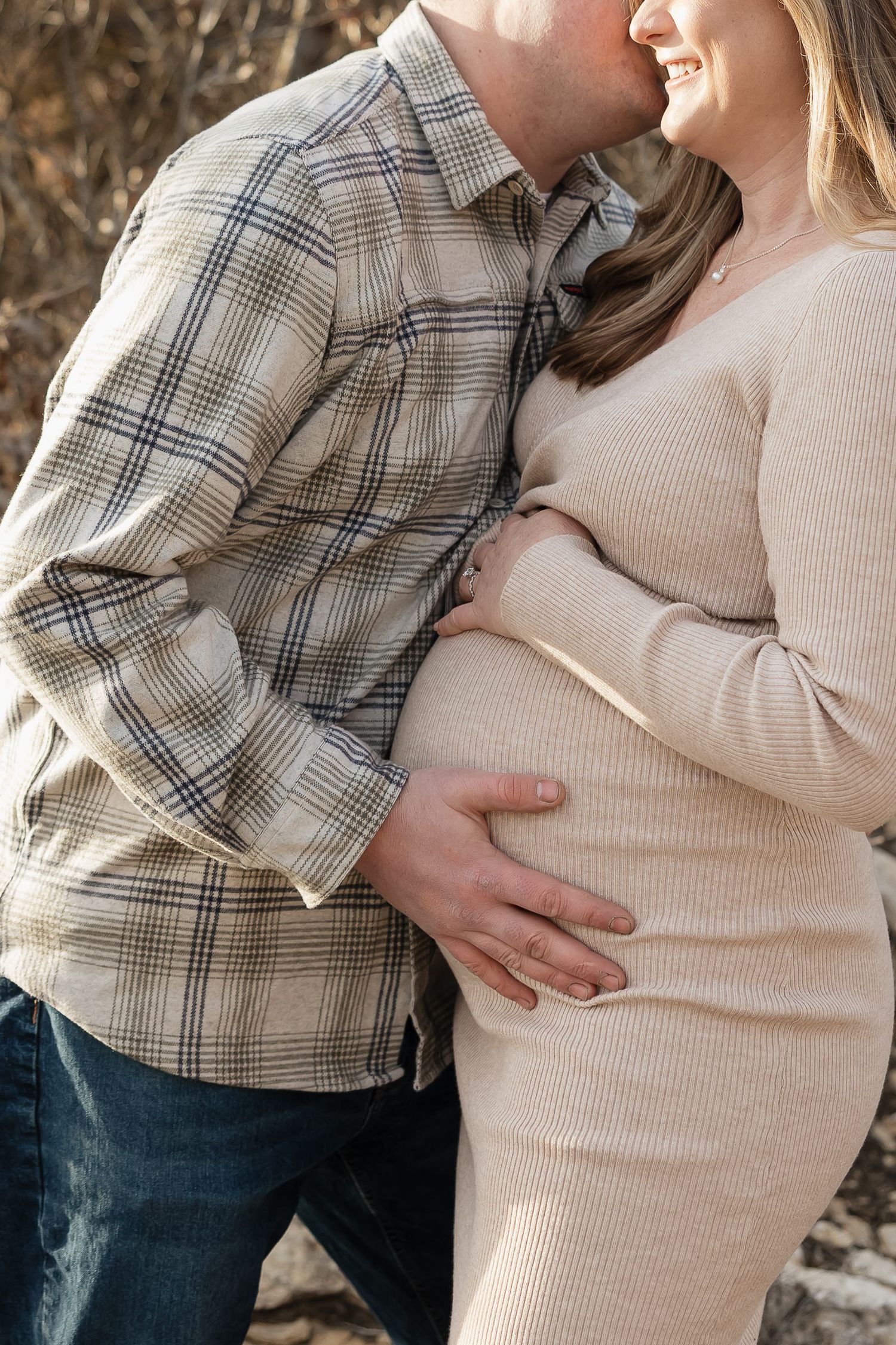 pregnant mother to be holds baby bump while dad kisses her cheek during photo session as date night ideas in kansas city