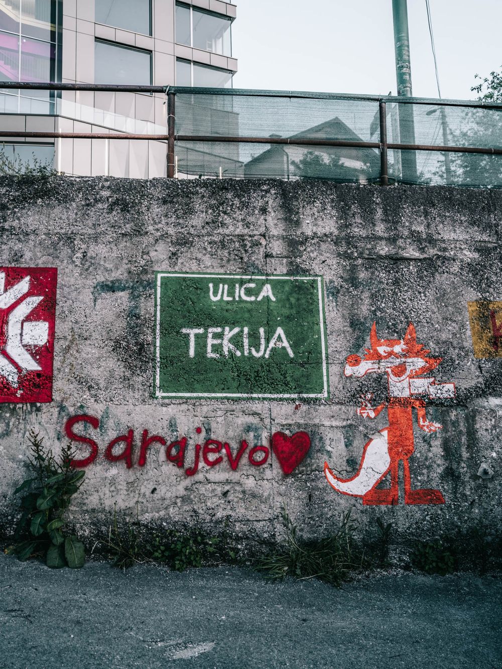 Sarajevo street sign for Ulica Tekija with graffiti mural and heart on weathered concrete wall.
