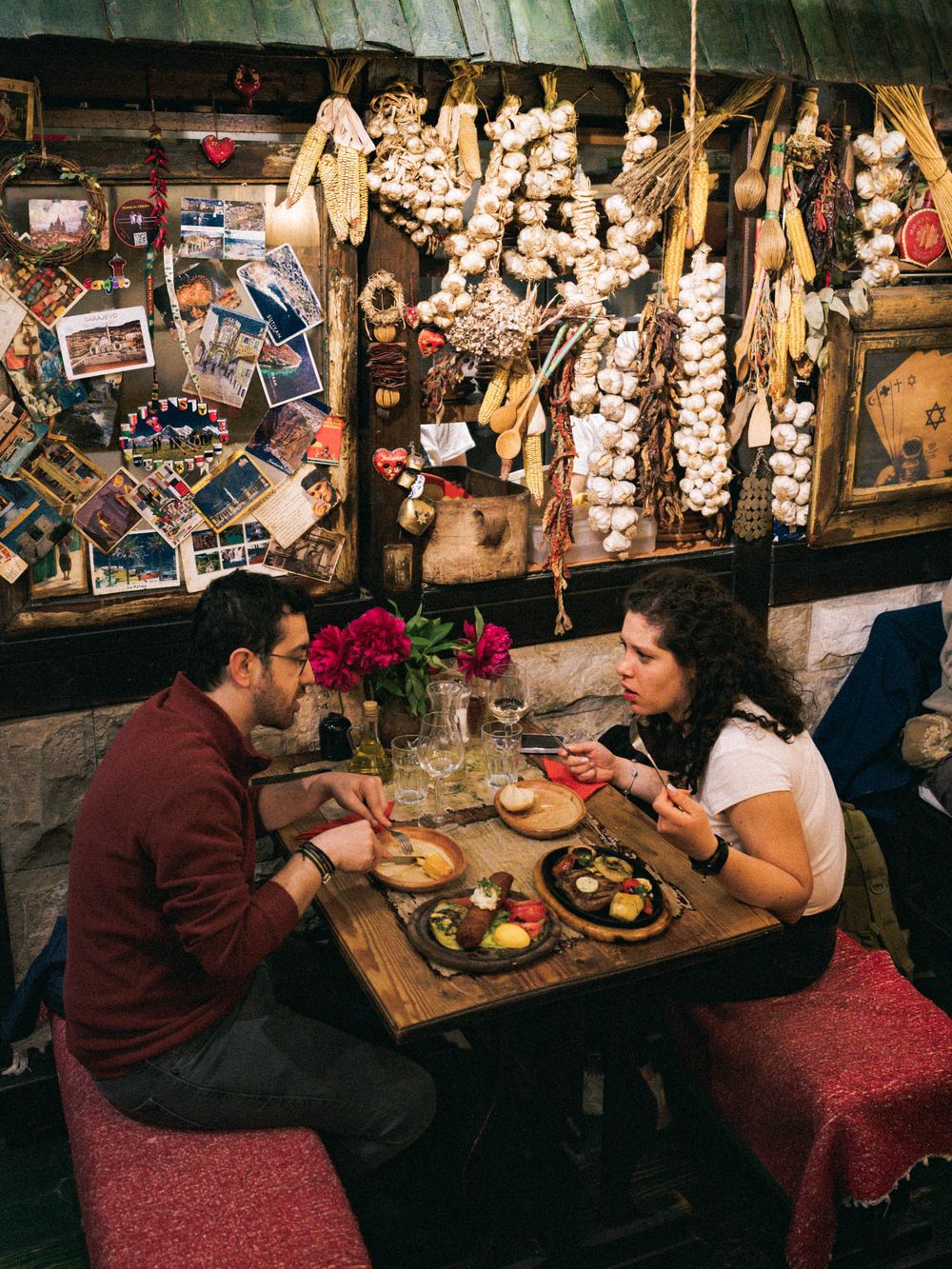Couple dining at rustic wooden table surrounded by hanging garlic and vintage decor.