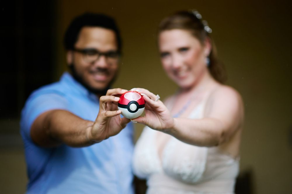 Bride and groom holding a Pokeball together at their Pokemon-themed wedding celebration.