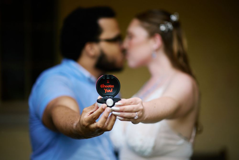 Newlyweds kissing while holding a Pokeball wedding ring box at their geeky themed wedding ceremony.