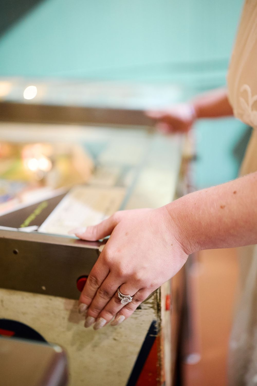 Close-up of a woman's hands with rings playing a vintage pinball machine in an arcade.