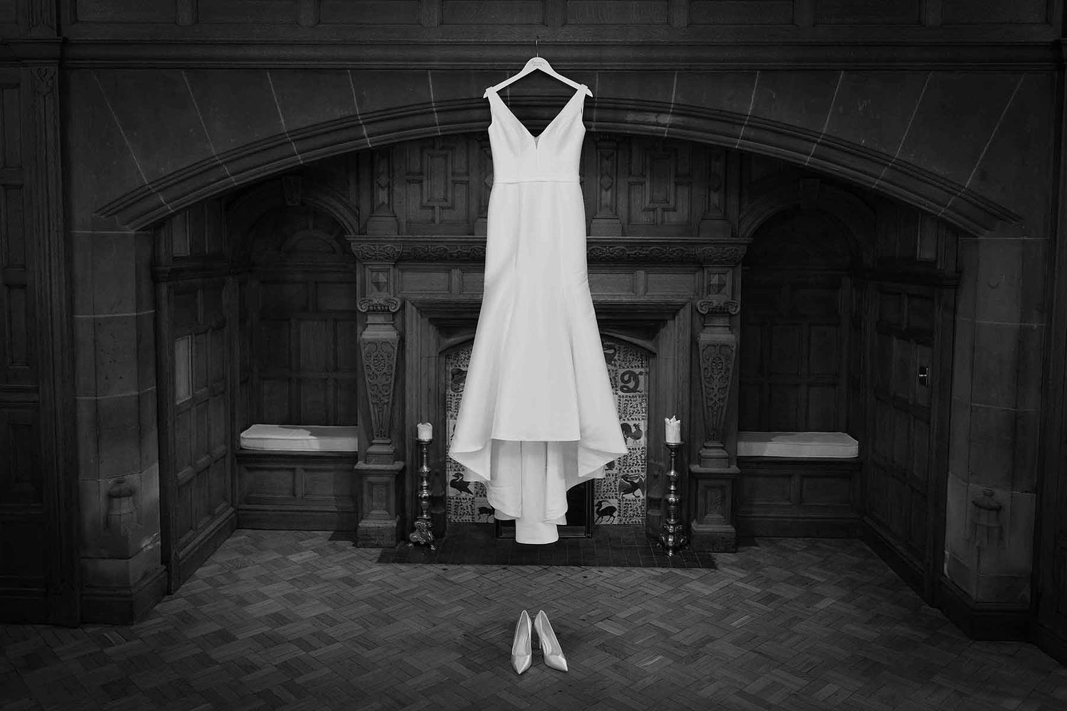 Black and white photo of a wedding dress hanging over a fireplace with bridal heels below it.