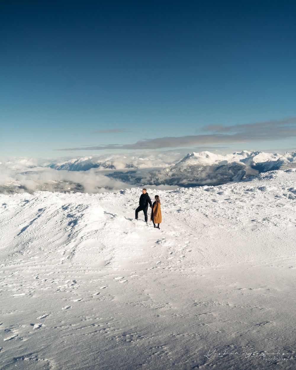 Couple standing together on vast snowy mountain summit with cloud-covered peaks below.

Vancouver Canada Scene