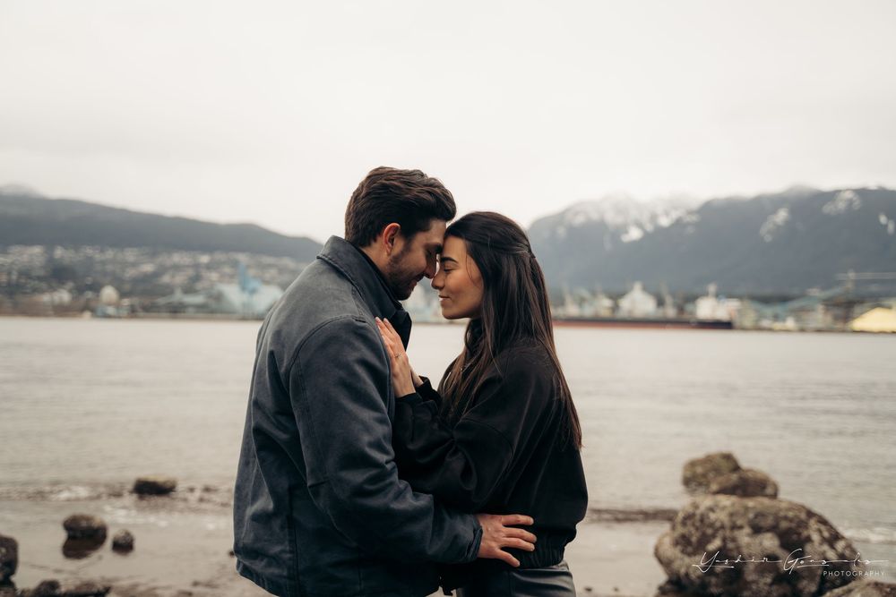 Romantic couple embracing near a rocky shoreline with snow-capped mountains and overcast sky in background.

Vancouver Canada Scene