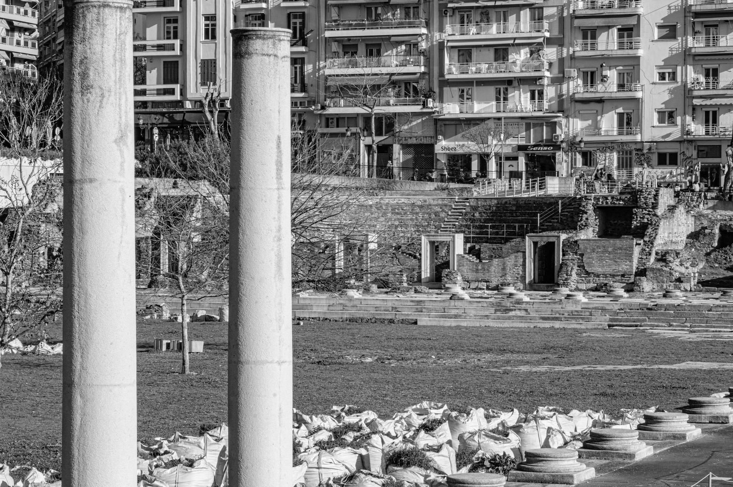 Ancient Roman columns and ruins stand in front of modern apartment buildings in a bustling urban area.