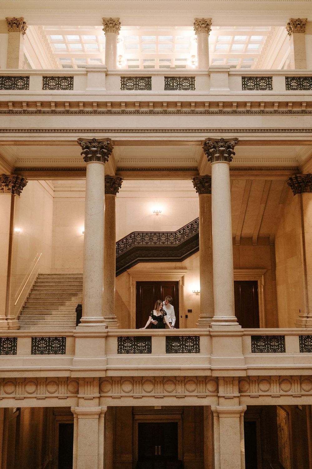Couple sharing intimate moment on balcony of grand neoclassical building with tall Corinthian columns.