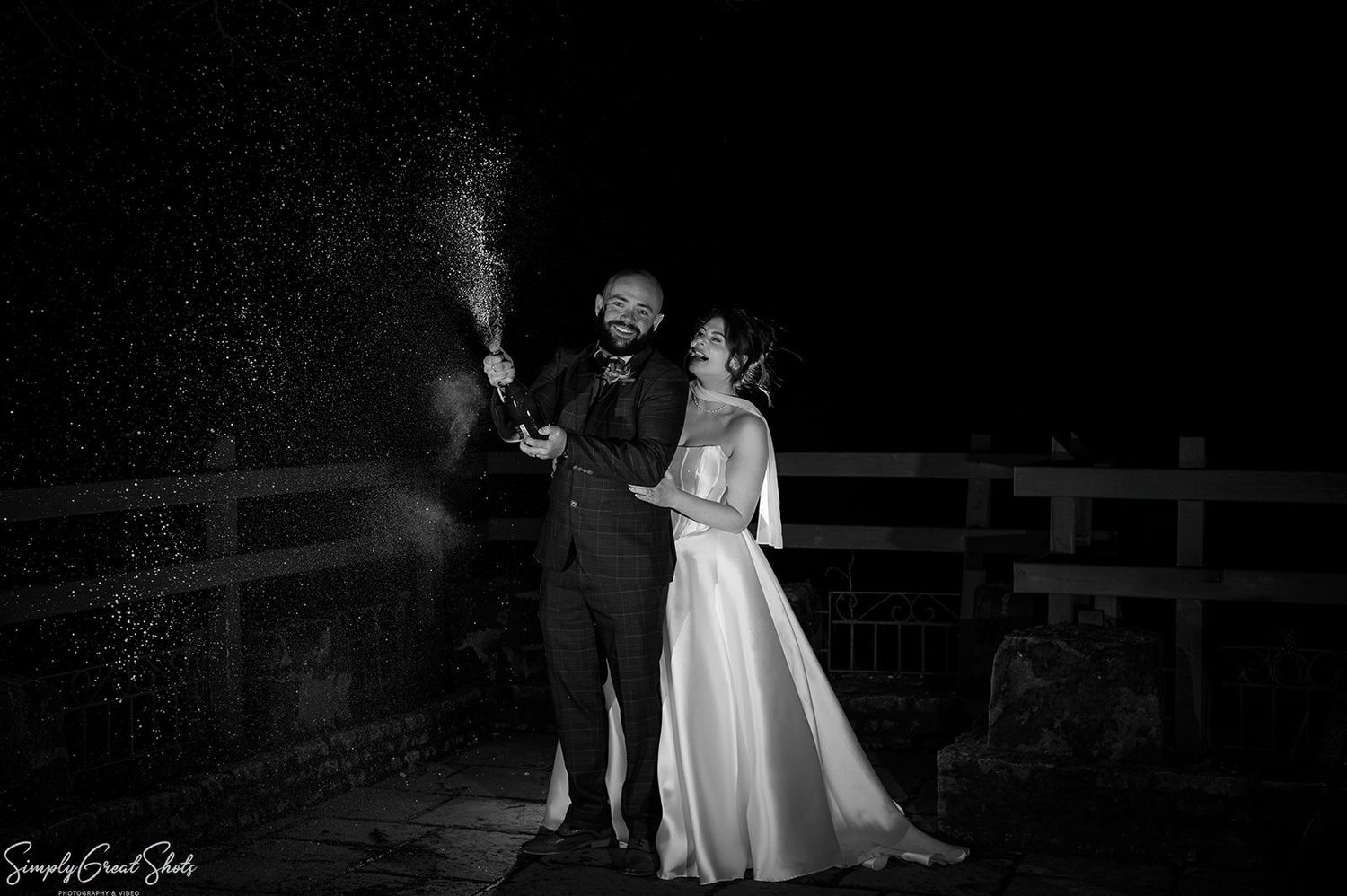 Bride Stacey and groom Jack spraying champagne at night at The Saxon Mill, Warwickshire. Valentine's Day wedding photography