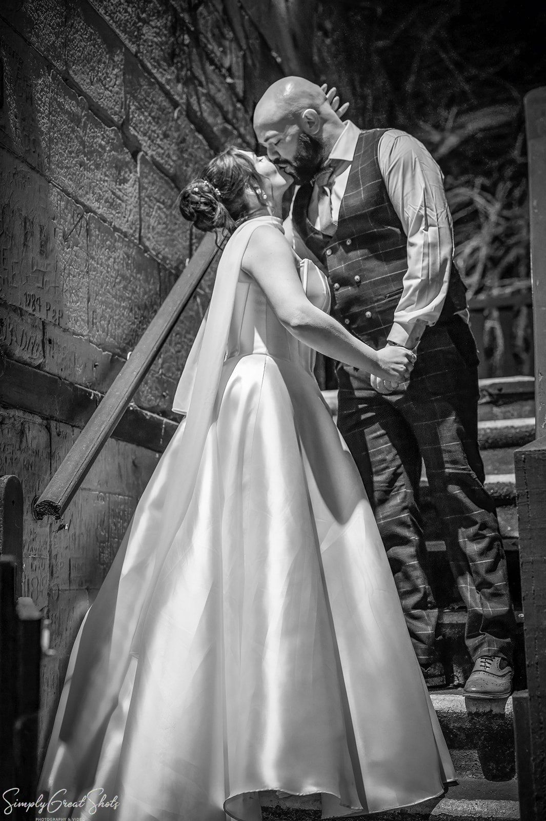 Black and white portrait of bride Stacey and groom Jack kissing on the stone staircase at The Saxon Mill, Warwickshire.