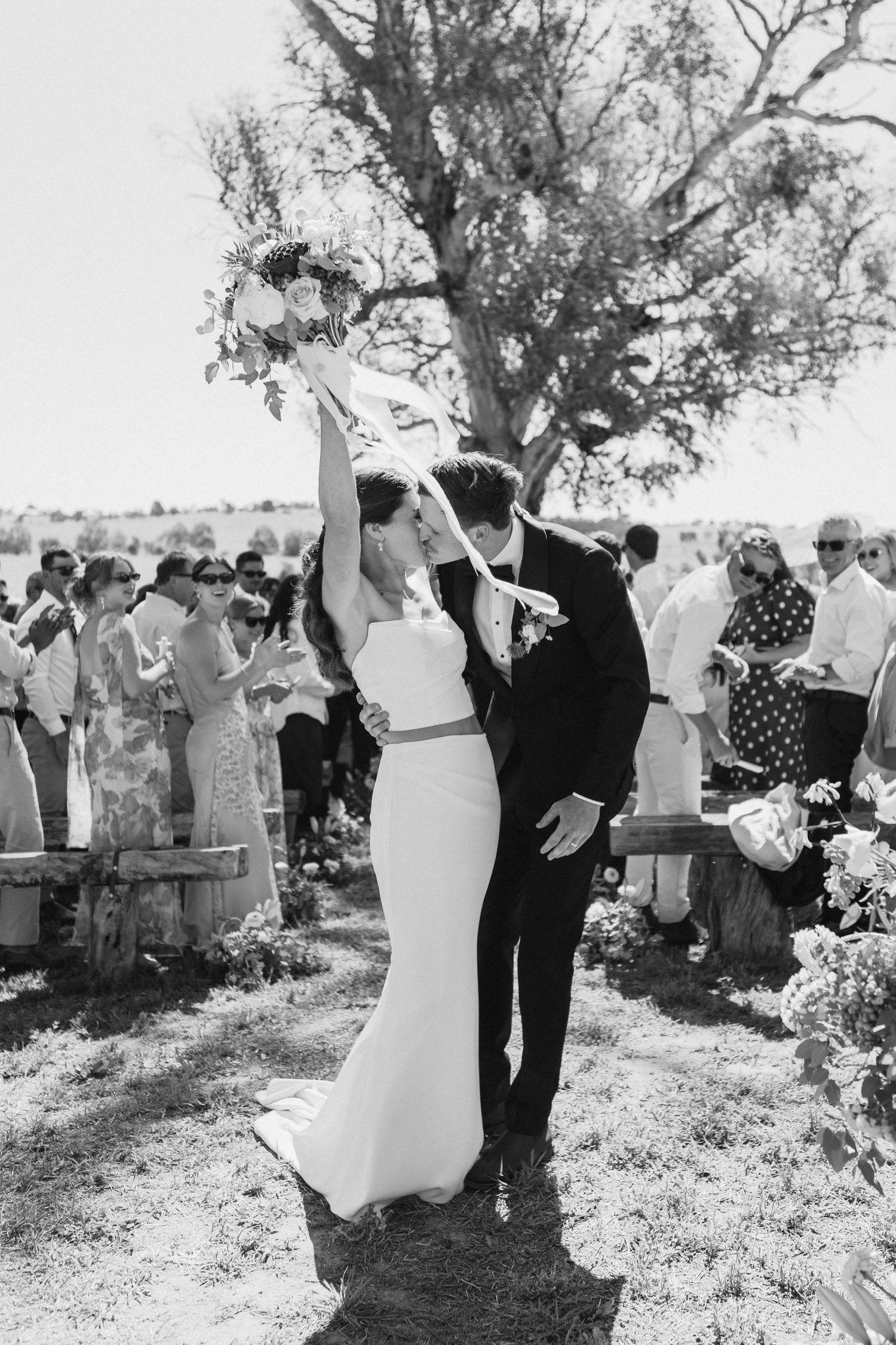 Bride and groom kissing and cheering with bouquet at the end of the aisle