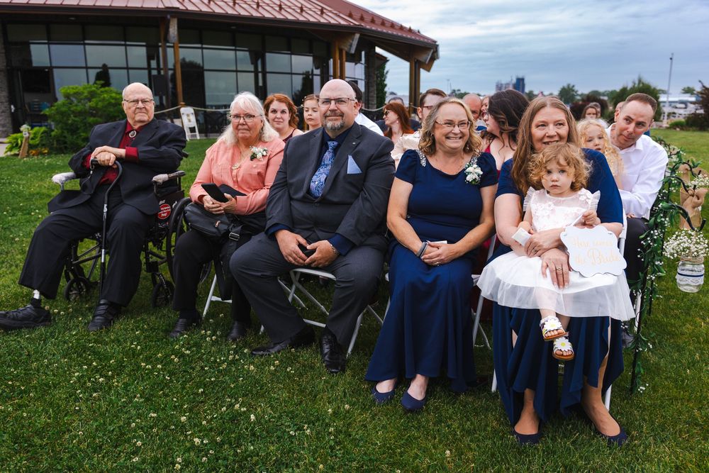 A group of wedding guests sitting together on the grass during an outdoor celebration.