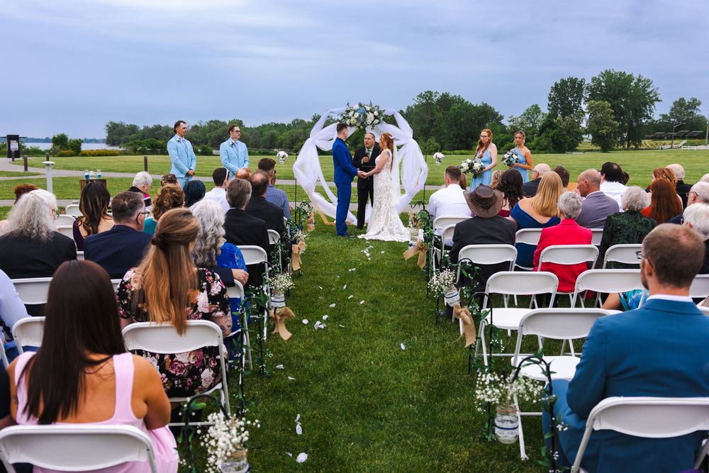 Guests seated in white chairs on a grassy lawn for an outdoor wedding ceremony with water views in the background.