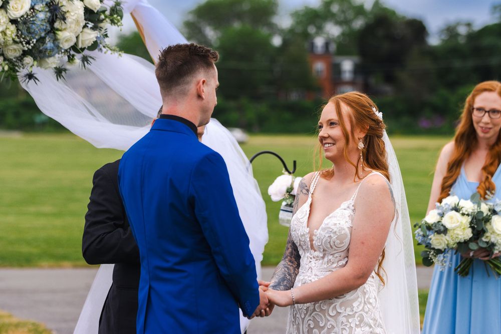 Wedding couple embraces outdoors surrounded by greenery and floral decorations during a summer ceremony.