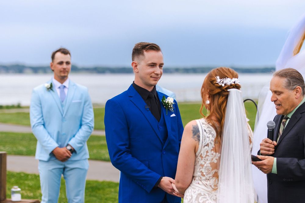 Outdoor wedding ceremony with guests gathered by a waterfront setting.