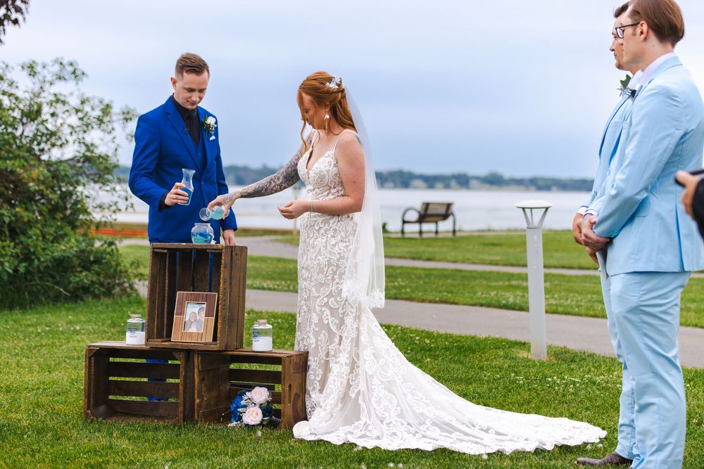 Wedding ceremony taking place on a waterfront lawn with rustic wooden decor elements.