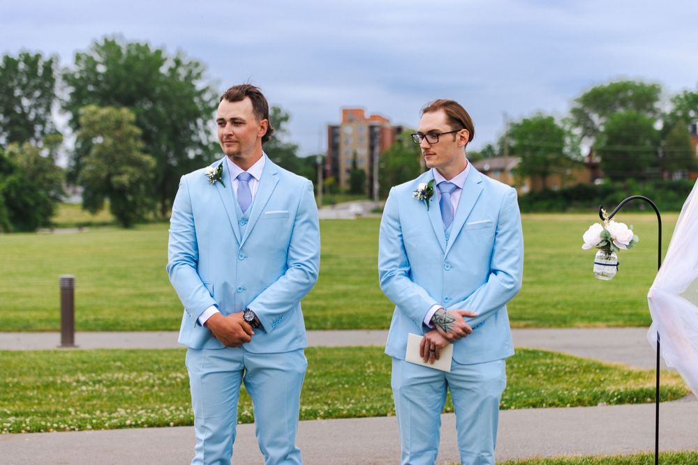 Groomsmen in matching powder blue suits stand together on a sunny lawn.