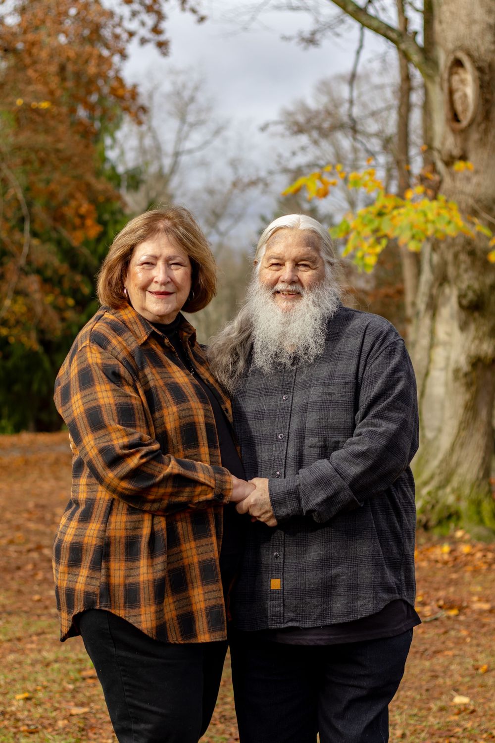 Smiling senior couple holding hands together in a beautiful autumn park with fall foliage.