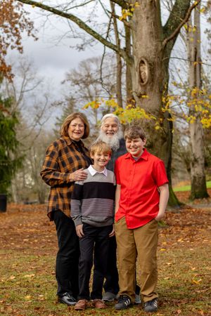 Grandparents with two grandsons smiling together in an autumn park with fall leaves.