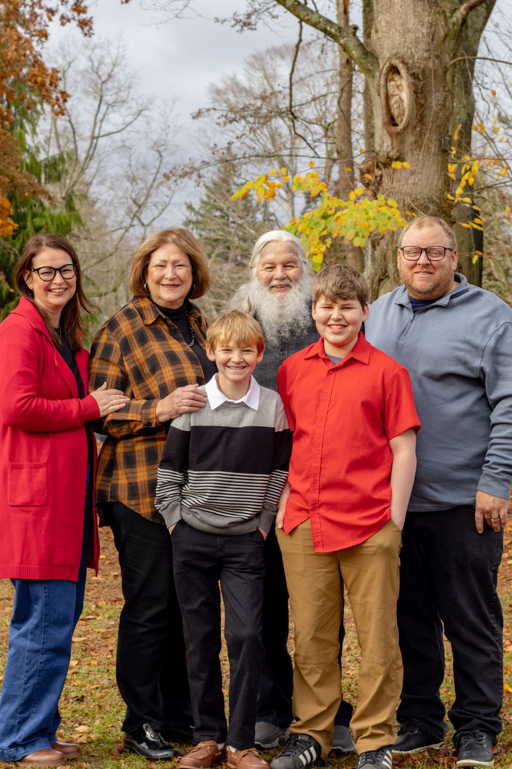 Multi-generational family of six posing together in autumn park with colorful fall foliage.