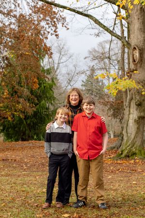 Grandmother posing with two young grandsons in an autumn park with colorful fall foliage.