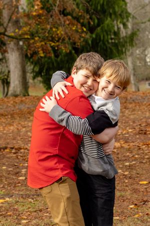 Two young brothers hugging and laughing together in a colorful autumn park setting.