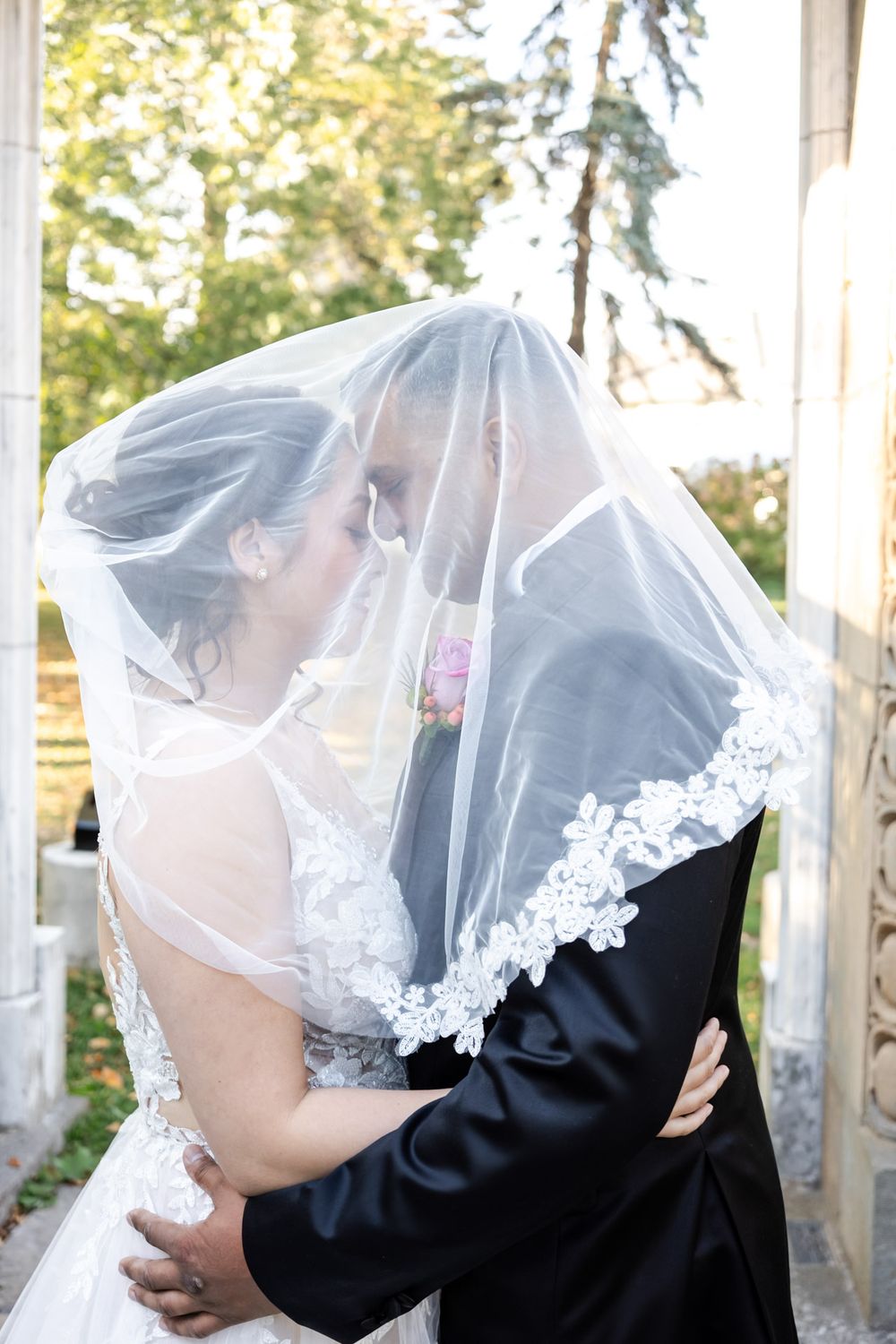 Bride and groom share an intimate moment under a lace-trimmed wedding veil outdoors.