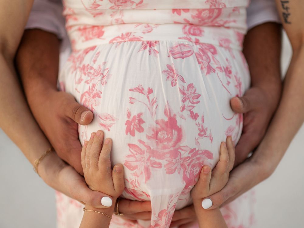Pregnant woman in floral dress with hands cradling baby bump, maternity photography concept.