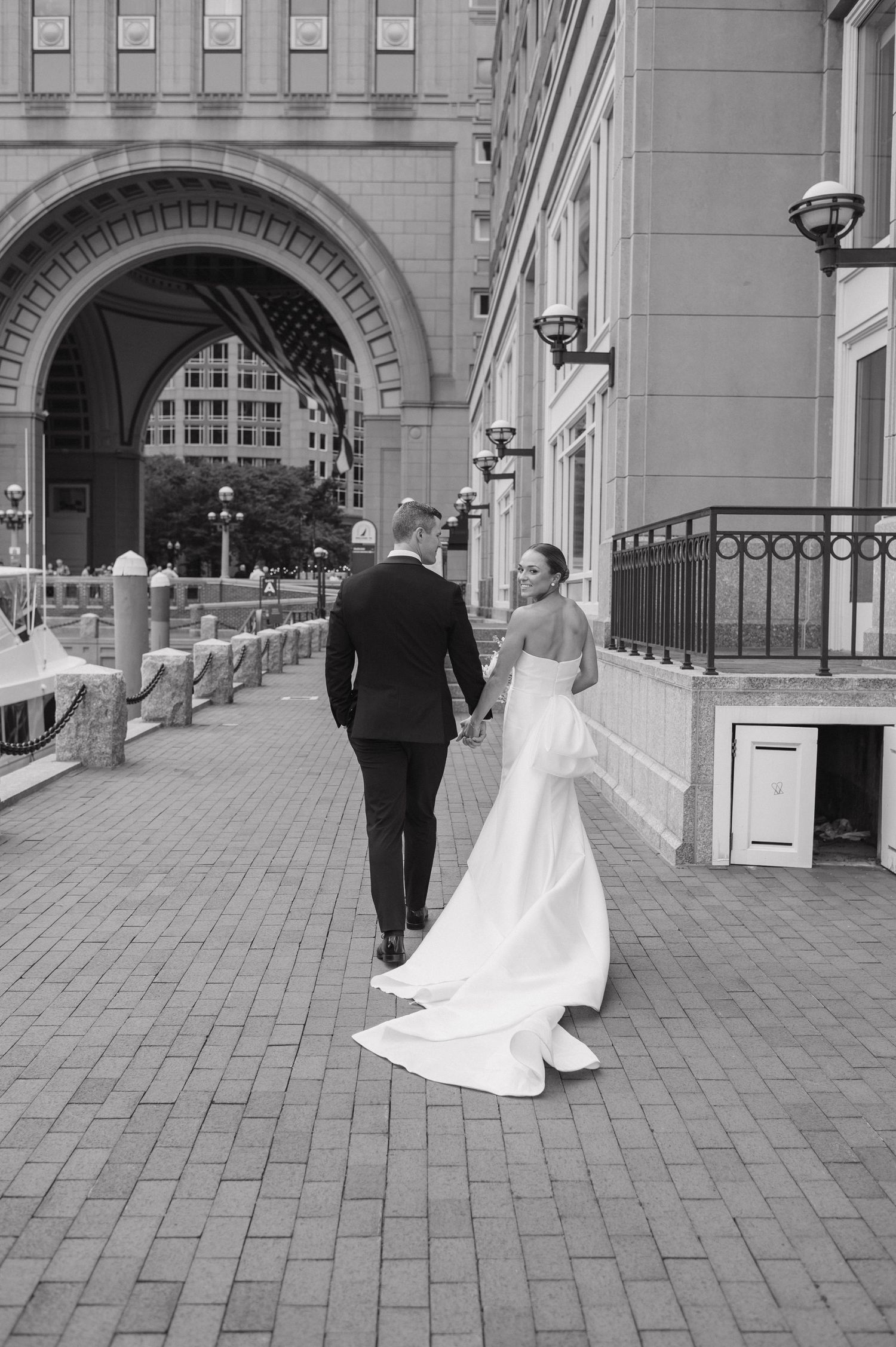 Black and white wedding sequence showing couple walking across brick courtyard with elegant archways and lamp posts.