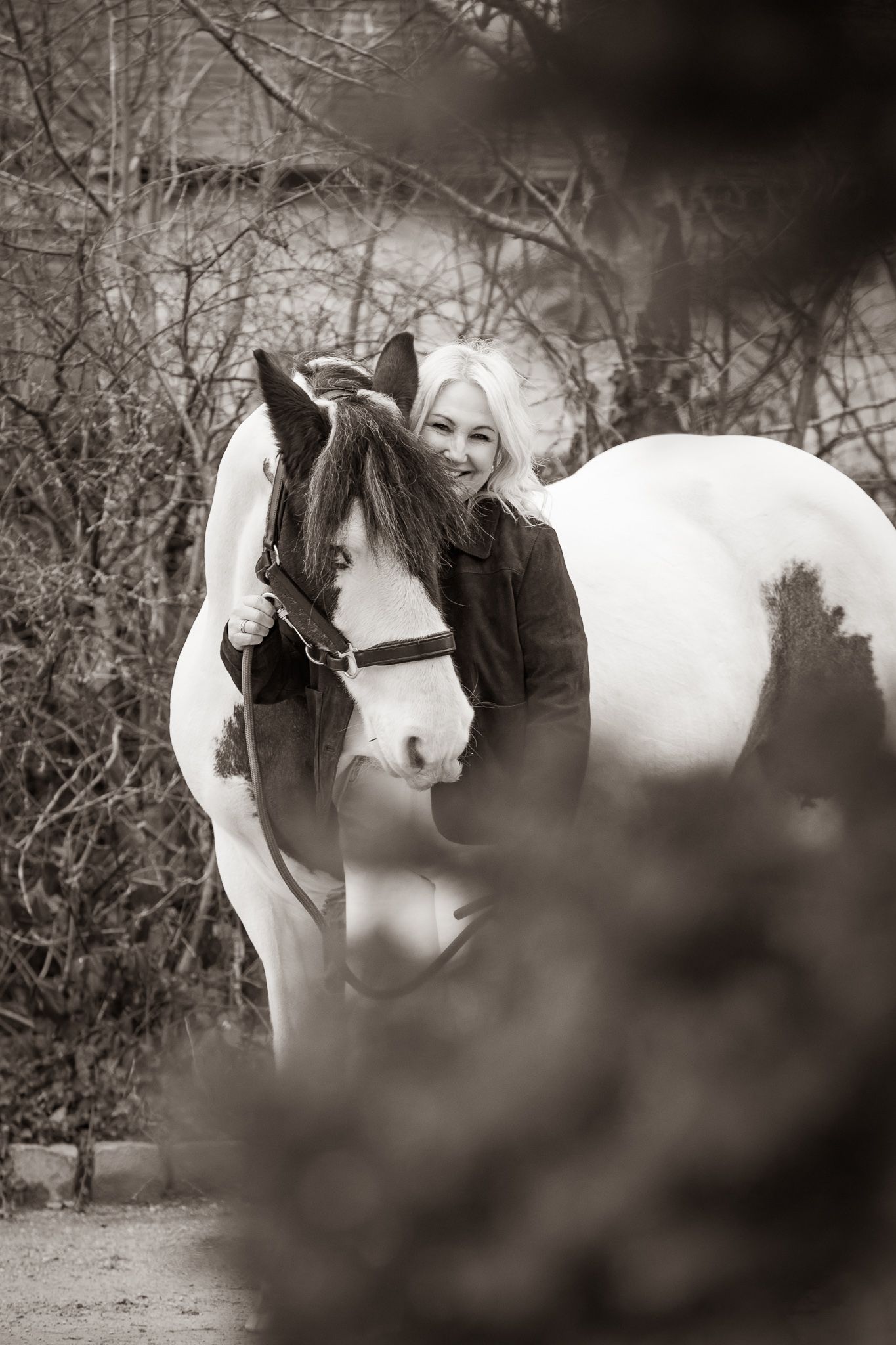 A brown horse and rider in a white sweater pose together against autumn foliage in soft natural lighting.