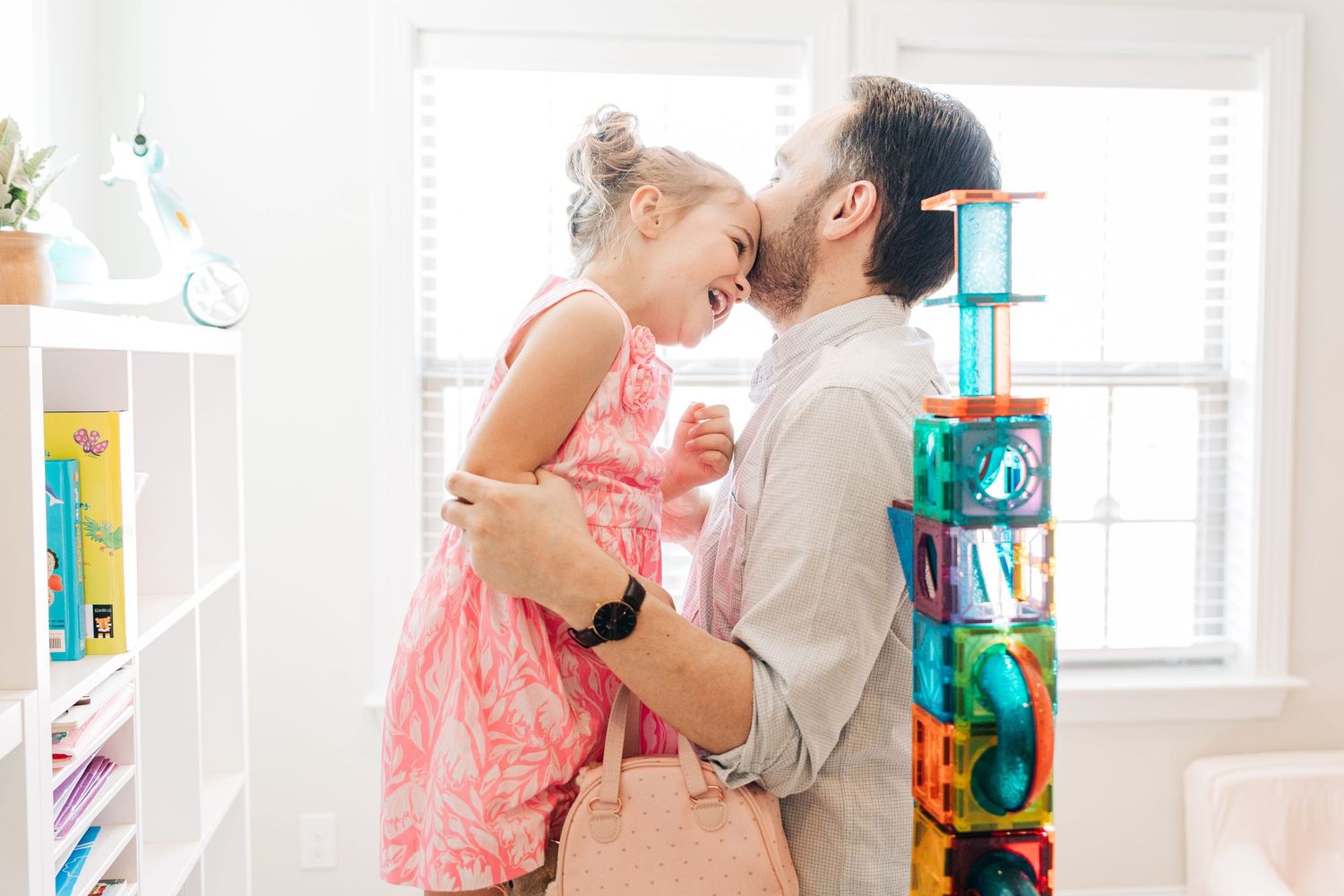 A parent and child share a tender moment while playing in a bright room with colorful toys and decorations.