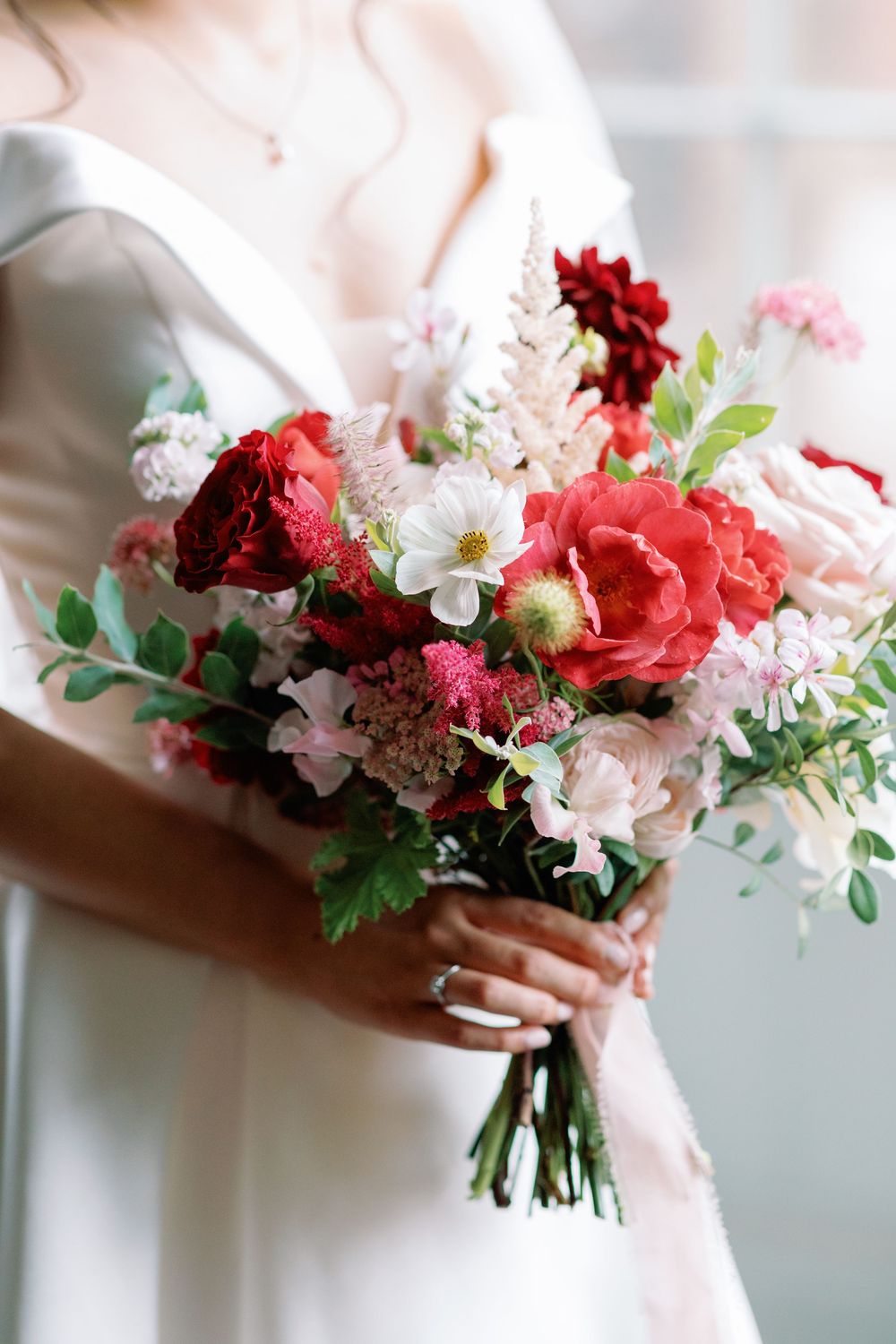A romantic bridal bouquet featuring deep red and soft pink flowers with delicate white blooms and cascading greenery.