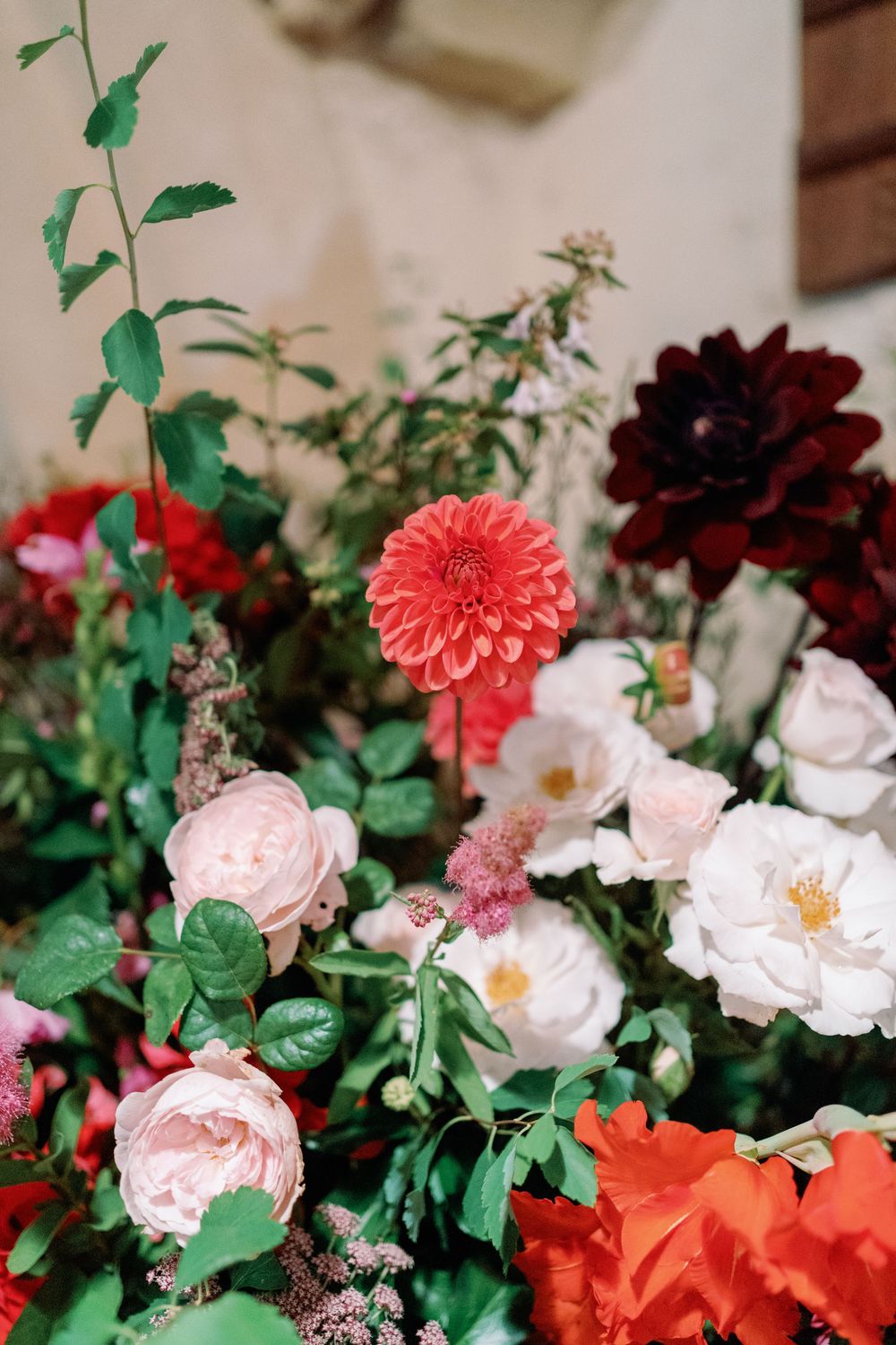 Elegant floral arrangement featuring coral dahlias, pink roses, and deep burgundy blooms with green foliage taken by Maddie Waters