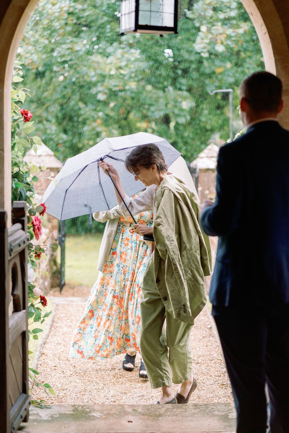 Wedding party walking under umbrellas along a covered church porch walkway.
