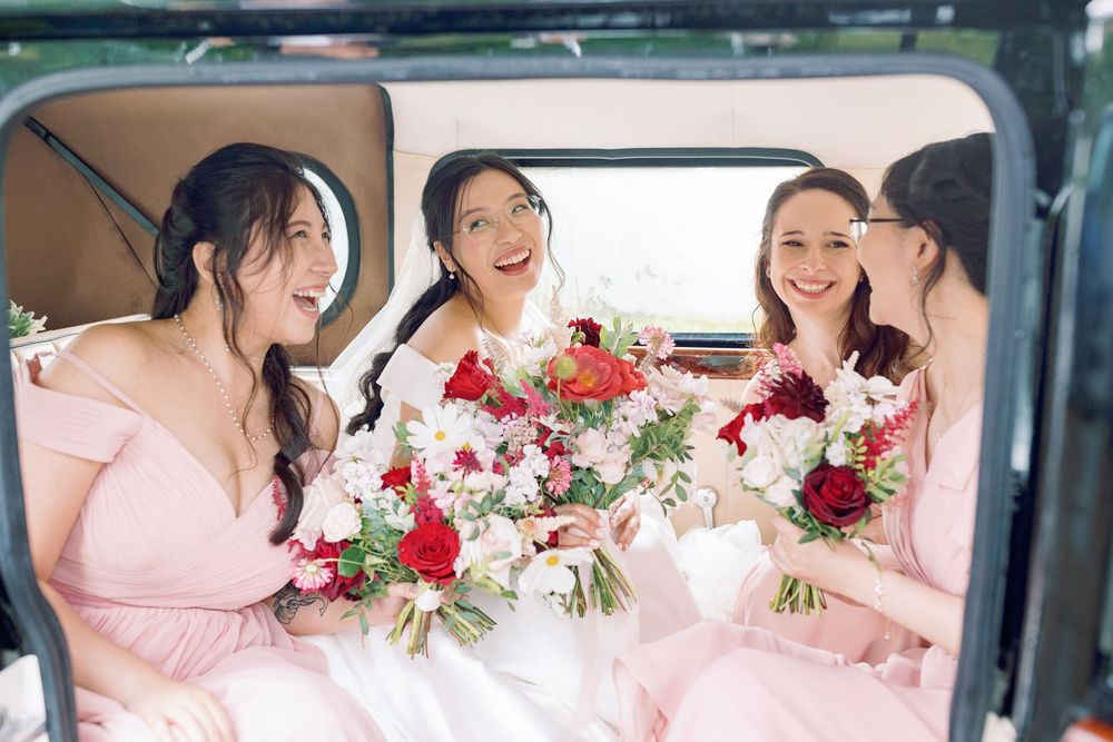 Bridesmaids wearing pink dresses pose together with red and pink bouquets inside a vintage wedding car taken by Maddie Waters Photography