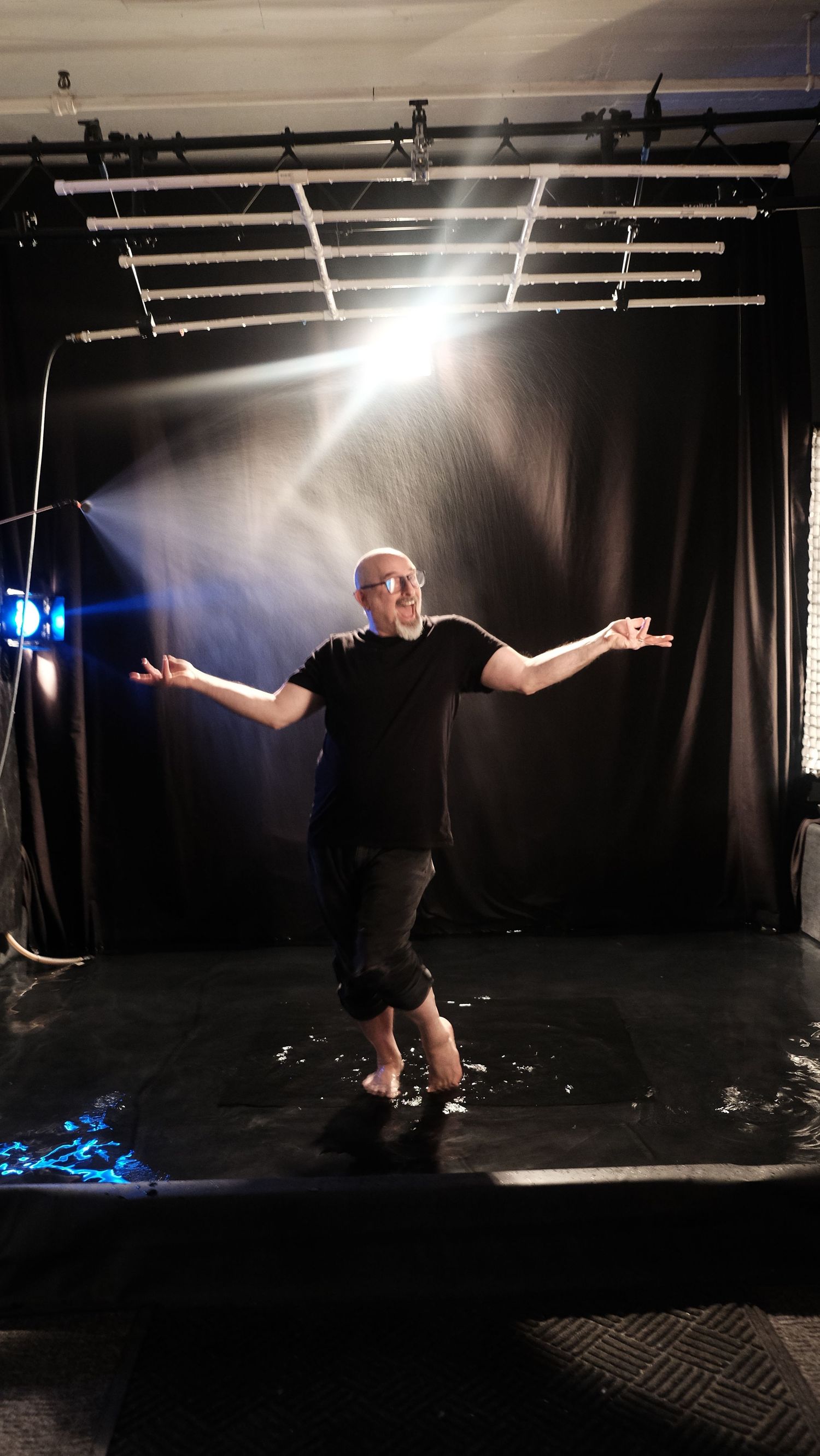 A dramatic sequence of a performer in black moving through spotlit darkness on a stage with theatrical lighting effects.