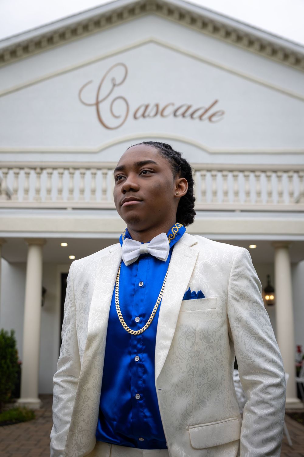 A person in a white tuxedo with blue vest stands in front of the Cascade venue entrance.