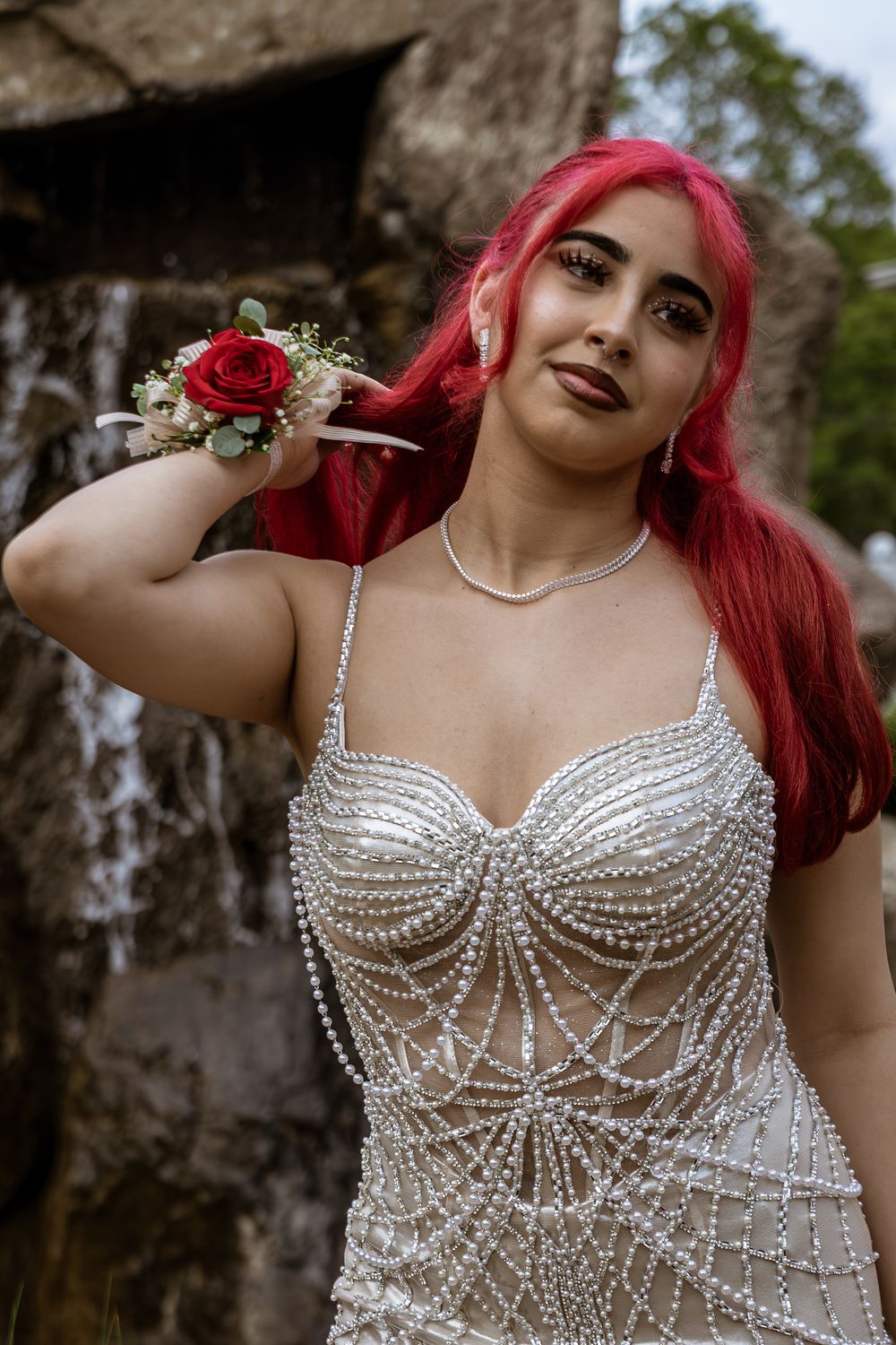 A model in a pearl-embellished white corset dress poses outdoors against a natural backdrop.