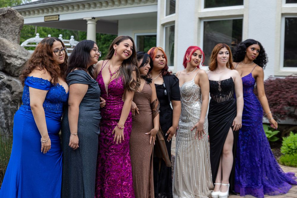 A group in formal evening gowns poses together outdoors in front of a building during a special occasion.