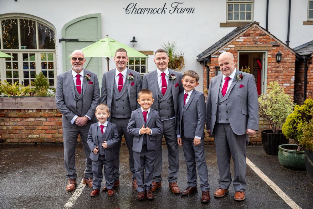 Groomsmen and pageboys in matching grey suits pose outside Charnock Farm wedding venue.