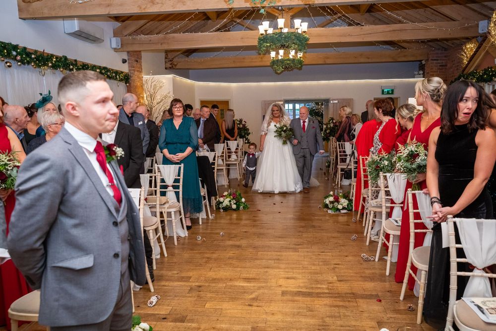 Bride walks down the aisle escorted by father at rustic barn wedding ceremony.
