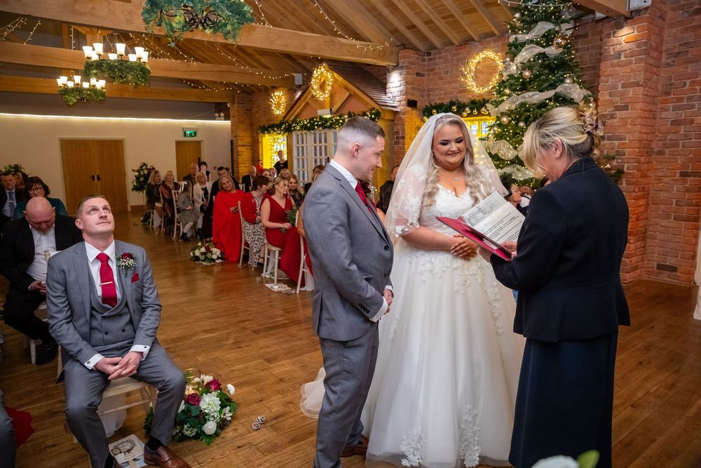 Bride and groom exchange vows before officiant at Christmas-decorated barn wedding ceremony.