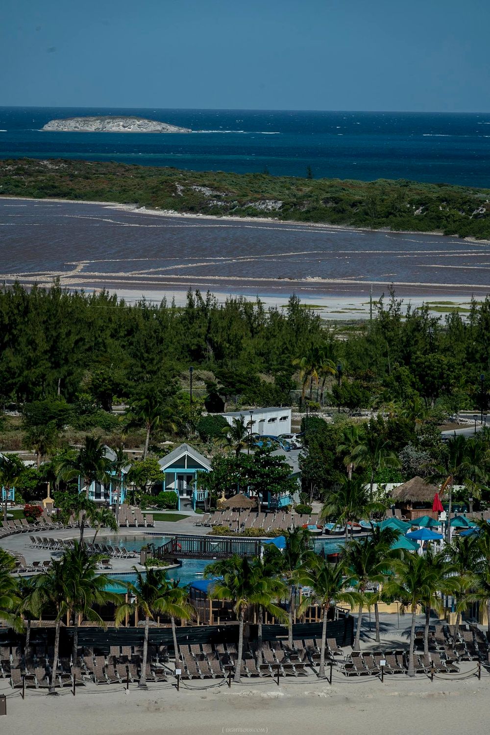 Aerial view of a tropical resort with pool, palm trees, and salt flats near a turquoise Caribbean sea.