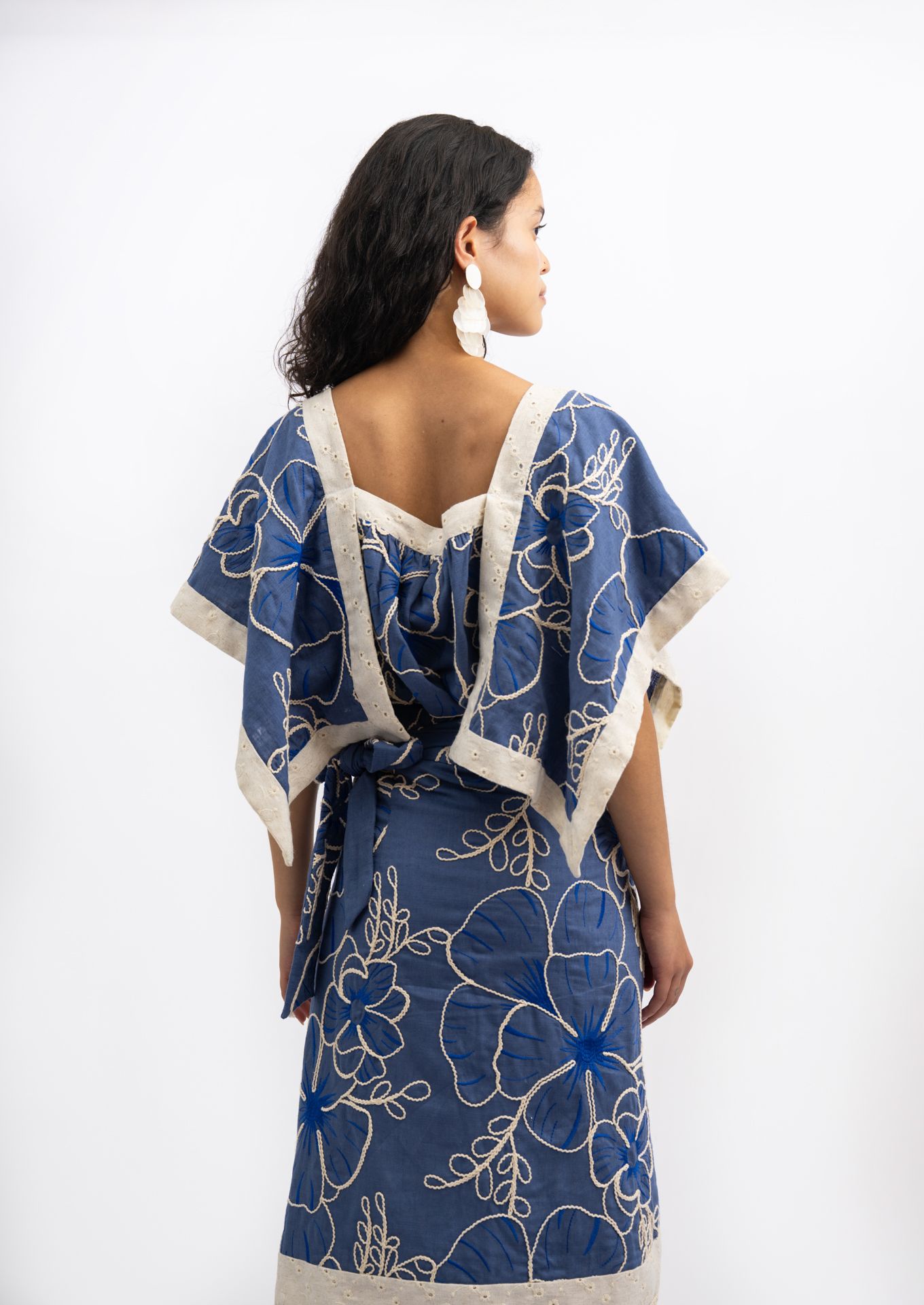 Woman wearing a blue floral kaftan dress with cream trim and open back, viewed from behind.