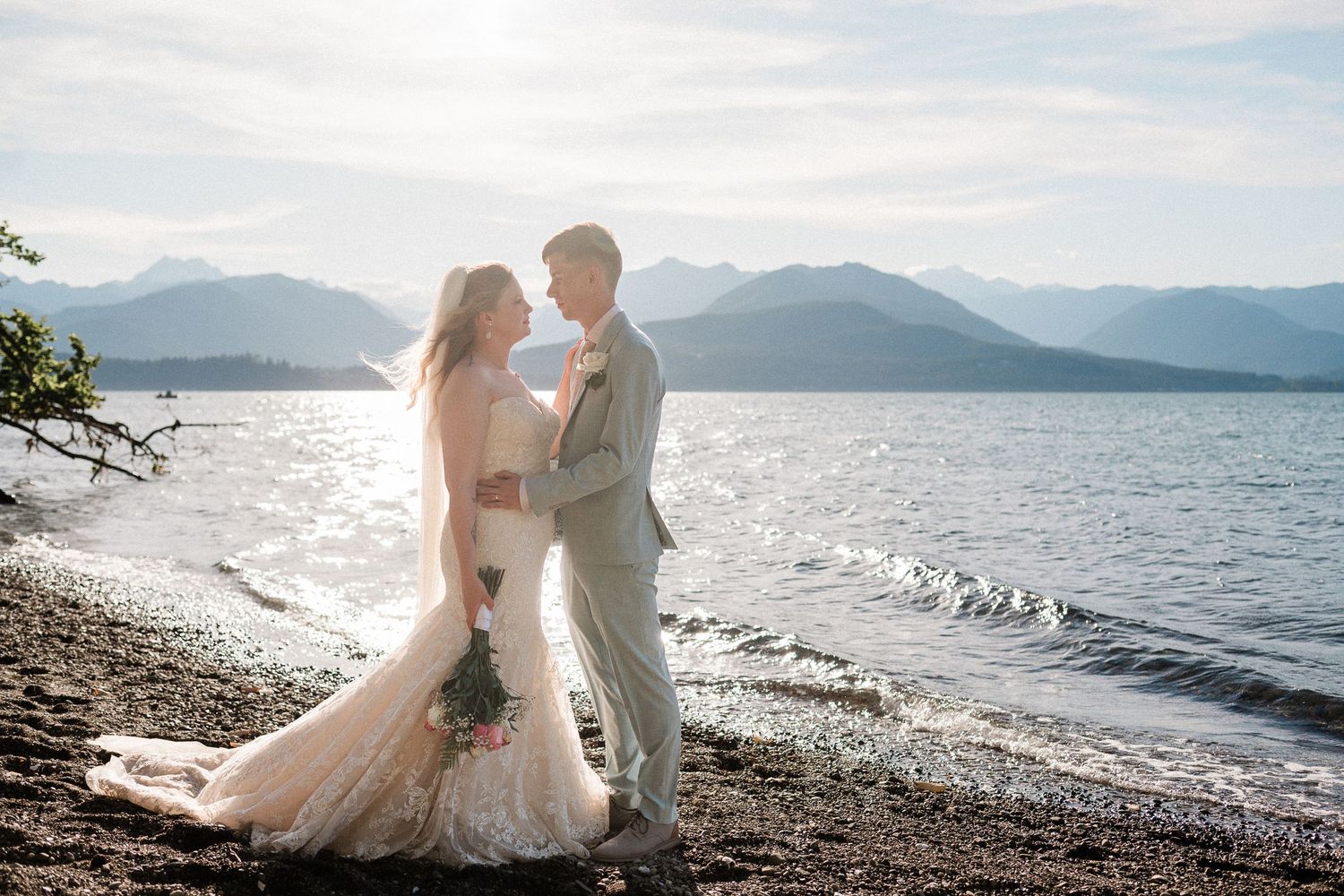 A couple walks in front of scenic mountain lake surrounded by evergreen forest and misty clouds reflecting in calm waters on a moody day.