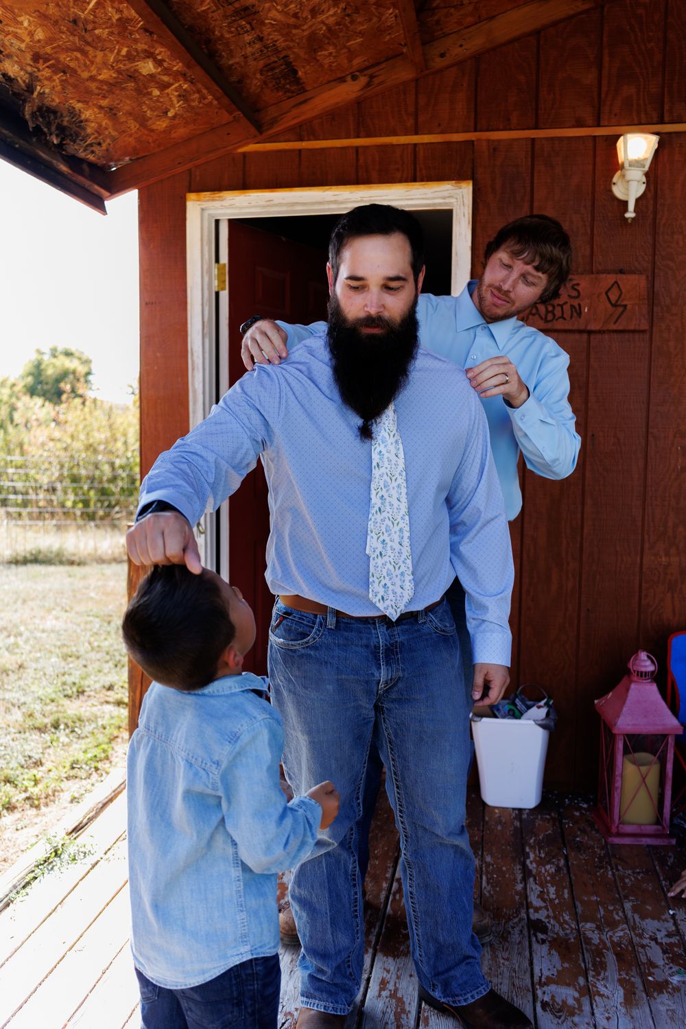 Groom and groomsmen in light blue shirts and jeans gathered on a wooden porch of a rustic cabin before a Montana wedding
