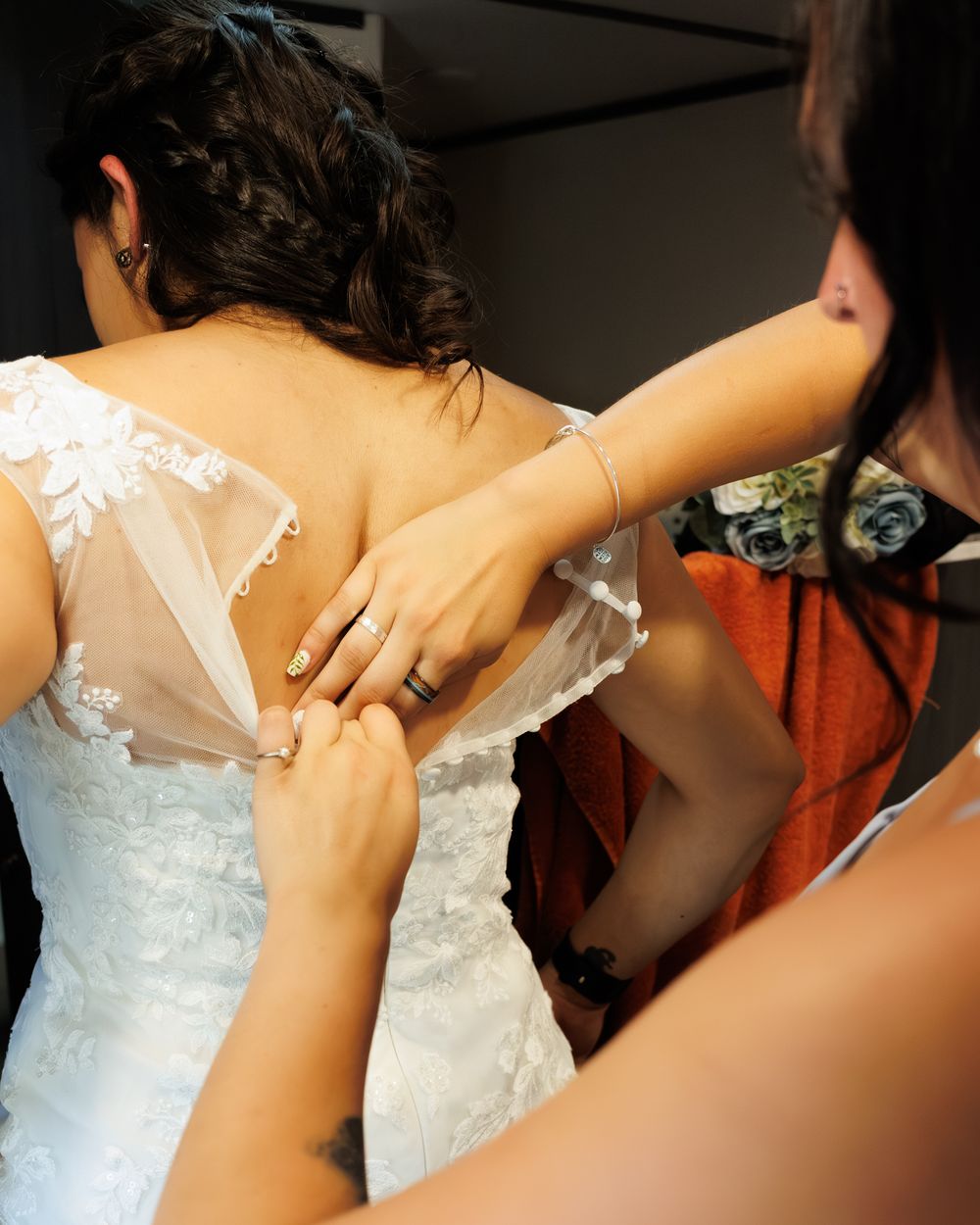 Close-up details of a bridesmaid helping the bride into her dress