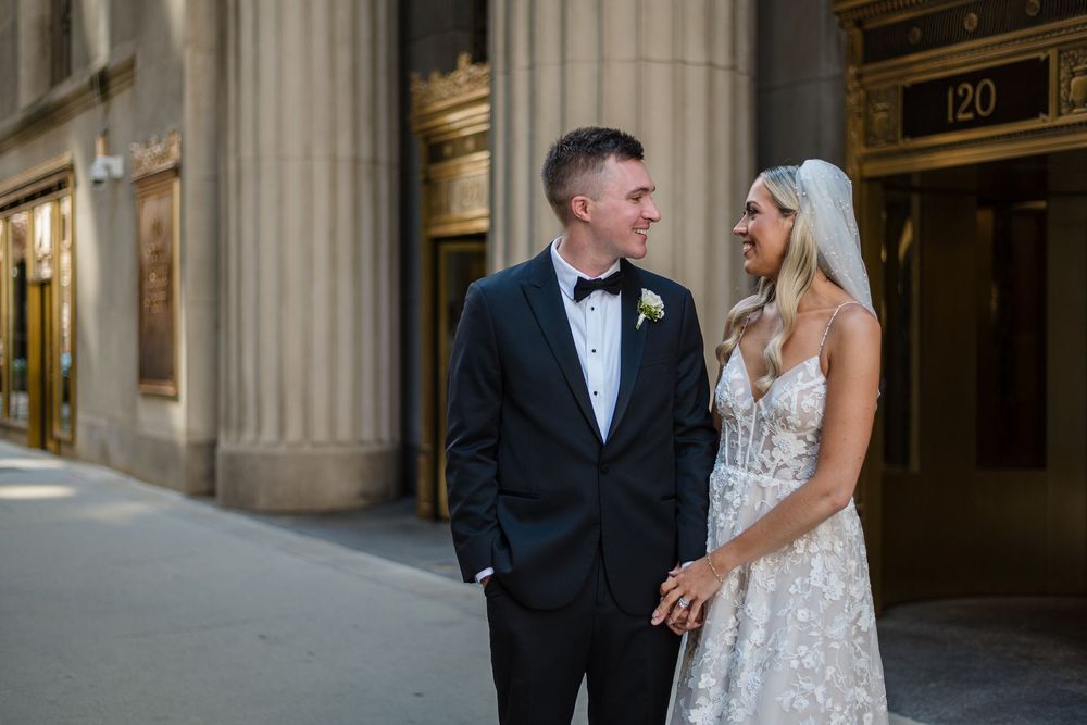 A couple in formal wedding attire share a joyful moment together in front of elegant stone columns.
