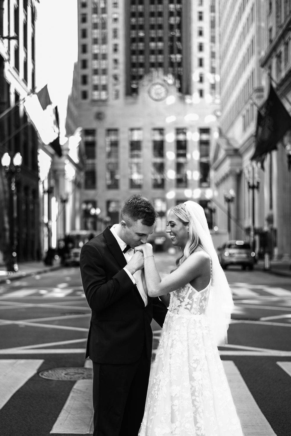 A black and white wedding photo sequence shows a couple dancing playfully on a city street with tall buildings in background.