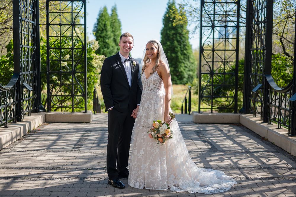 Bride and groom share a romantic moment under a wrought iron archway in a lush garden setting.