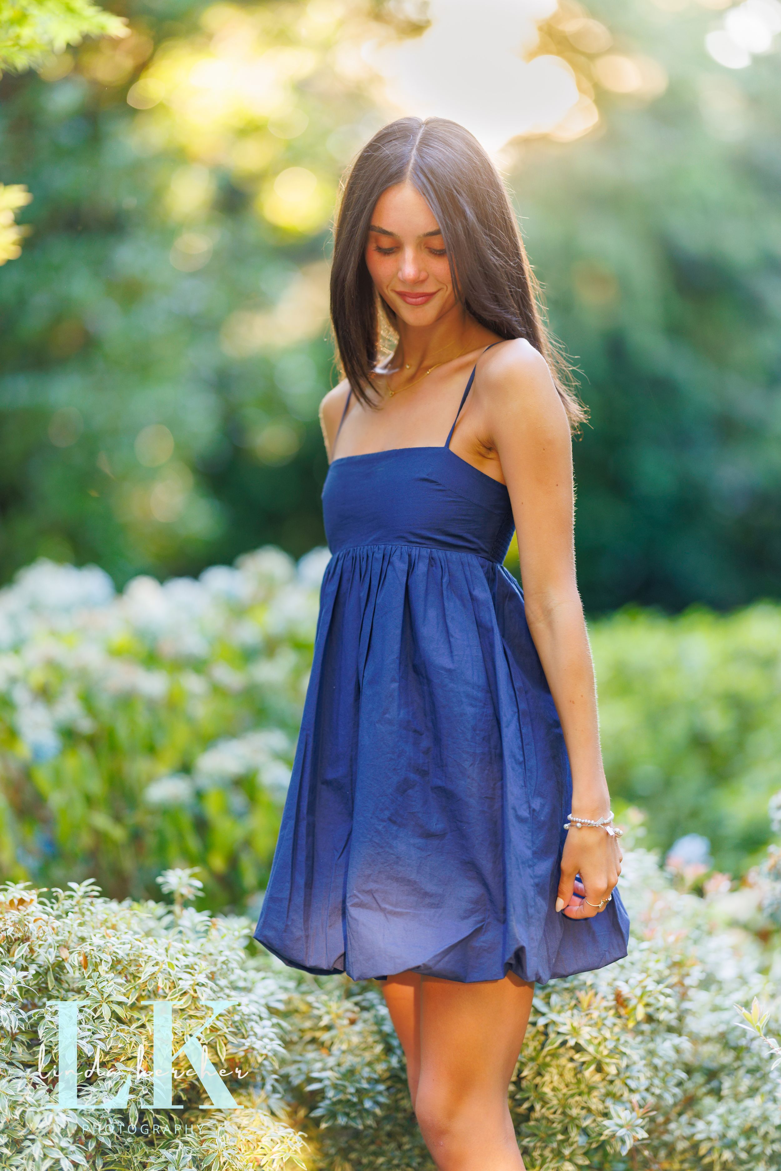 Young woman in navy blue sundress standing among white wildflowers in a sunlit garden.